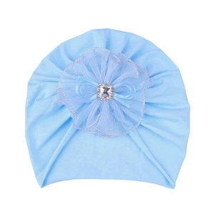 Détail d'un turban bébé avec grande fleur en dentelle, strass et nœud en ruban bleu