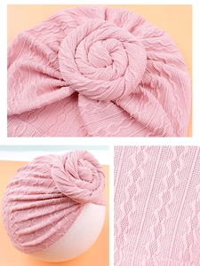 Close-up of pink knit baby turban featuring a large spiral flower knot and cable stitch