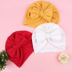 Détail de bonnets turbans pour bébés en jaune, rouge et blanc avec grands nœuds