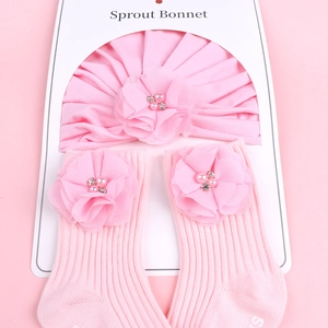 Détail d'un ensemble bonnet et chaussettes roses avec fleurs en mousseline et perles