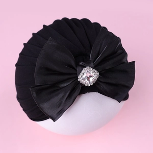 Détail du turban noir pour bébé orné d'un grand nœud en strass sur fond rose