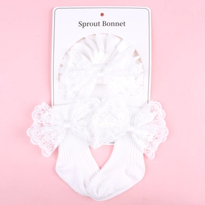 Close-up of white knitted baby socks and lace bow headband set on a pink background