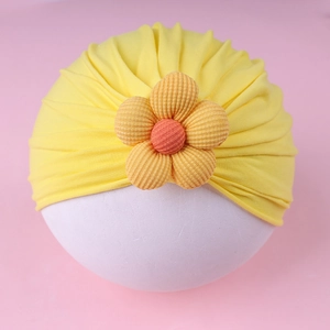 Detail of baby turban featuring a bright yellow pleated fabric and 3D floral decoration