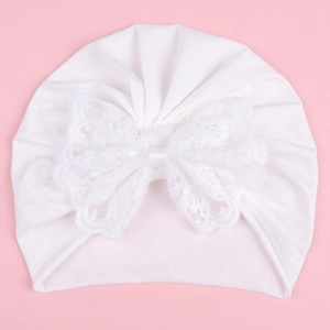 Detail of white infant beanie with a large lace embroidery bow on pink background