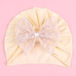 Detailed view of baby turban hat with a large white lace bow on soft yellow knit fabric