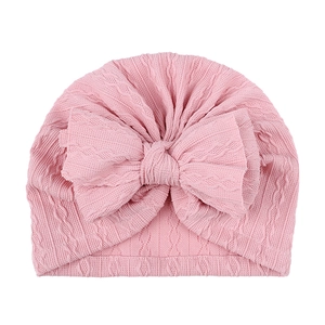 Vue détaillée du bonnet en maille rose pour bébé avec un grand nœud en tissu doux