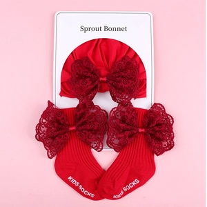 Detail of red baby turban and socks set with delicate lace bows on pink background