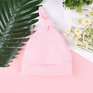 Close-up of soft cotton pink newborn knot hat with decorative white daisy and green leaf