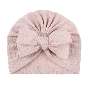 Détail du bonnet en tricot rose pour bébé avec motif torsadé et grand nœud décoratif