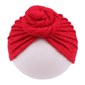 Detailed texture of red knitted baby turban hat with a top knot on a white background