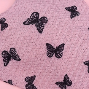 Detail of pink waffle fabric featuring black butterfly embroidery on breathable textile