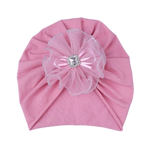 Close-up of pink baby turban hat featuring lace flower, ribbon bow and faux diamond