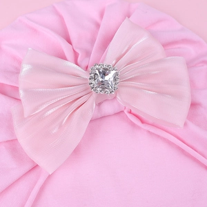 Vue détaillée du bonnet rose pour bébé avec nœud en satin et décoration en strass
