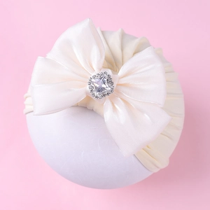 Détail d'un turban crème pour bébé avec gros nœud en satin et centre en diamant brillant