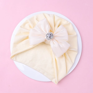 Détail du bonnet de bébé avec grand nœud en organza blanc et strass sur fond rose tendre