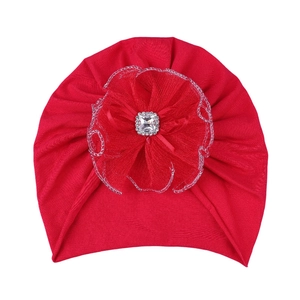 Detailed view of red knitted baby turban hat with large tulle flower and crystal center