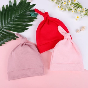 Three soft cotton newborn knot hats in red and pink colors shown on a decorative surface