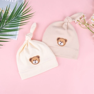 Detailansicht zweier weicher Baby-Strickmützen in Beige und Rosa mit Bären-Stickerei
