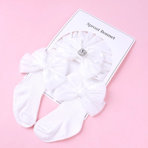 Vue détaillée du bandeau bébé blanc avec nœud en soie et chaussettes antidérapantes