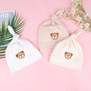Nahaufnahme von drei weichen Baby-Strickmützen mit süßen Braunbären-Stickereien