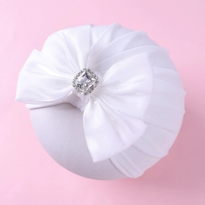 Détail d'un bandeau bébé avec unifié pour bébé avec grand nœud en satin blanc et ornement diamanté