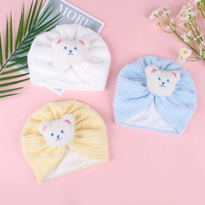 Detail view of baby beanies in white, blue, and yellow with teddy bear embroidery