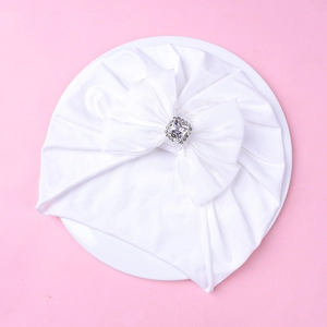 Détail d'un turban blanc pour bébé avec un nœud multicouche orné d'un diamant brillant