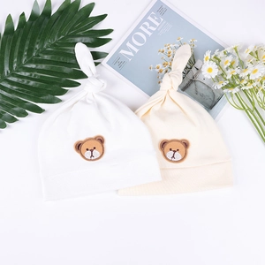 Detail von Baby-Knotenmützen in Weiß und Beige mit süßer Bärenbestickung