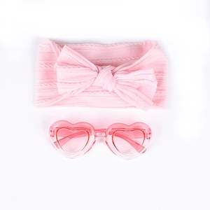 Détail du bandeau rose tricoté pour bébé avec nœud et lunettes de soleil en cœur