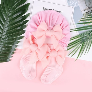 Set berretto e calzini rosa per neonata con grandi fiocchi in seta su sfondo pastello