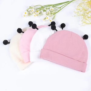 Présentation à plat de bonnets tricotés pour bébés en quatre couleurs avec pompons noirs