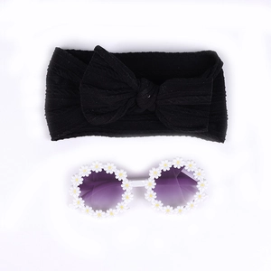 Détail d'un bandeau bébé à nœud noir et lunettes de soleil ornées de marguerites blanches