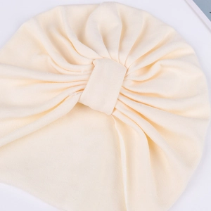 Close-up of off-white newborn turban hat with ribbed texture and front bow detail