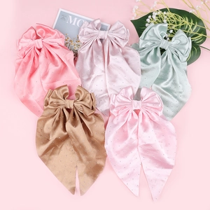 Détail de barrettes à nœuds en satin rose vert et violet ornées de petits strass brillants
