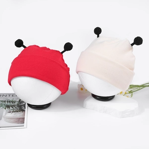 Détail de bonnets tricotés pour bébé en rouge et beige avec pompons noirs sur mannequins