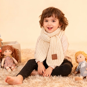 Detail of soft cream knitted scarf for kids featuring a brown leather branded patch