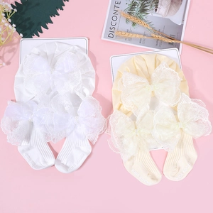 Detailaufnahme von Baby-Mütze und Socken mit großen Spitzenschleifen und Kunstperlen
