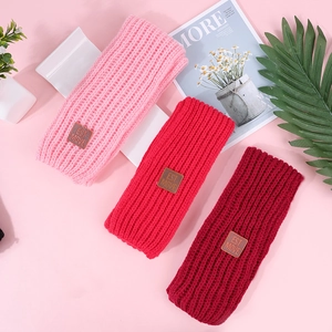 Detailed view of three knitted baby headbands in shades of pink and red with leather tags