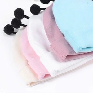 Détail de bonnets tricotés pour bébé empilés avec pompons noirs en cinq couleurs douces