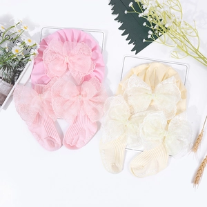 Flachbild von Baby-Baumwollmützen und Socken mit Spitzenschleifen in Rosa und Beige