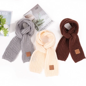 Detailed texture of chunky knit scarves in grey, beige, and brown with leather patches