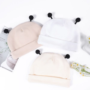Détails de la maille et pompons mignons sur ces bonnets pour bébé en crème et blanc