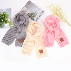 Detail of knitted baby scarves in three colors with leather label and soft ribbed texture