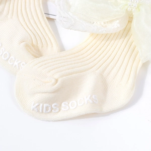 Detailansicht cremefarbener Babysocken mit Satin-Schleifen, Perlen und rutschfester Silikonsohle
