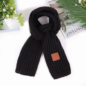 Detail of black chunky knit scarf featuring a brown leather label with EST MOVE engraving