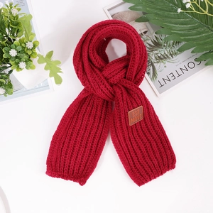 Detail shot of burgundy chunky knit scarf featuring a brown leather label and vertical ribs