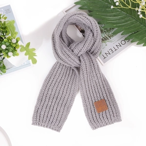 Flat lay of gray chunky knit children's scarf with a brown leather logo patch