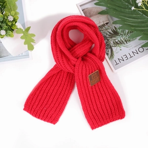 Detail of red chunky knit scarf featuring a brown leather brand tag on white surface