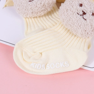Detail of beige ribbed baby socks with plush bear head and non-slip dotted grip soles
