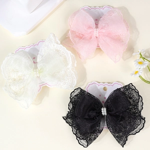 Close-up of lace ribbon bow hair clips with pearls in pink, white, and black colors